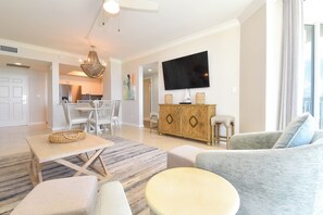 A modern living room with a dining area, a TV mounted on the wall, and a kitchen in the background.