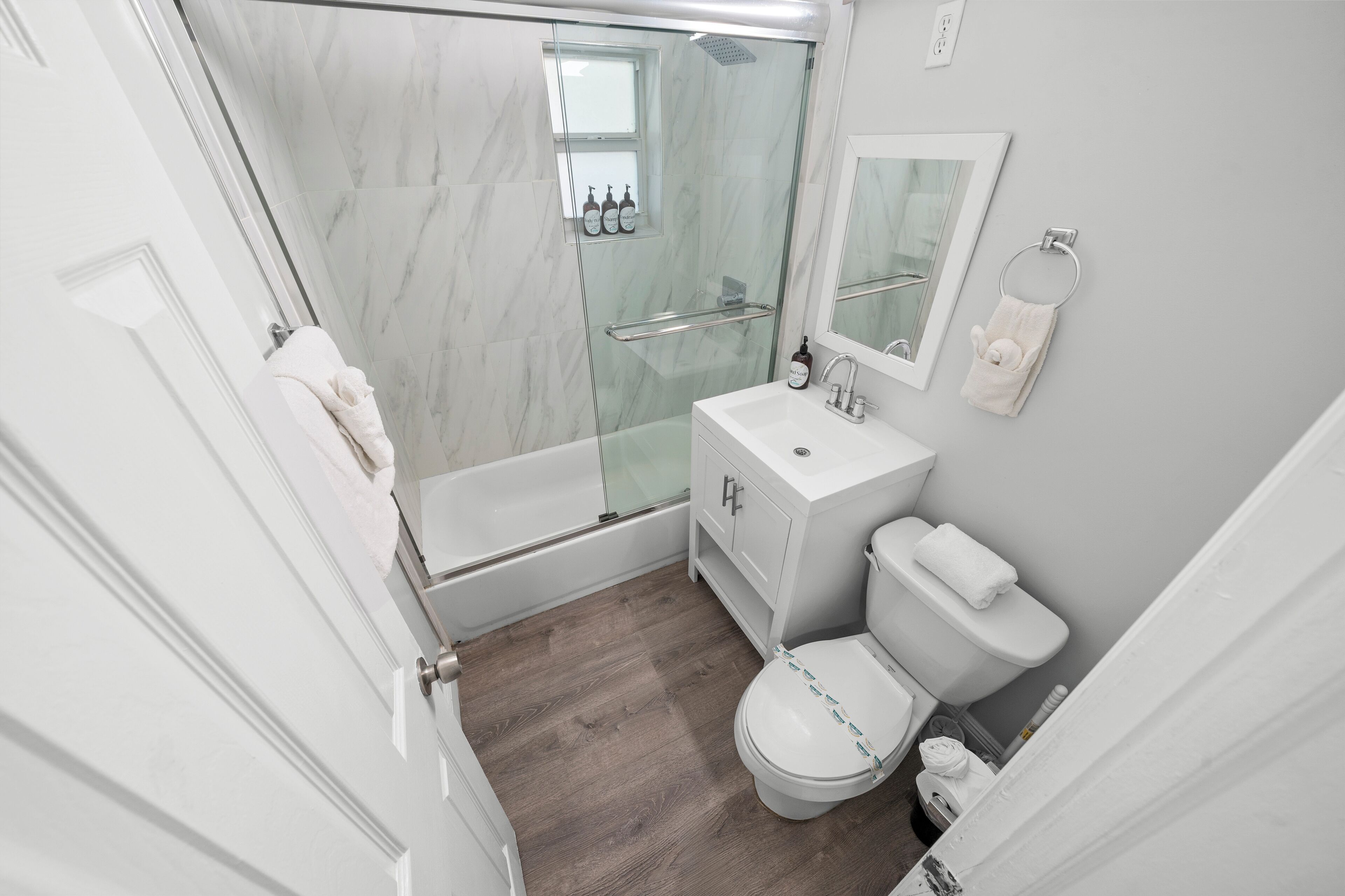 A modern bathroom with a glass-enclosed shower, a white sink, a toilet, and a mirror.