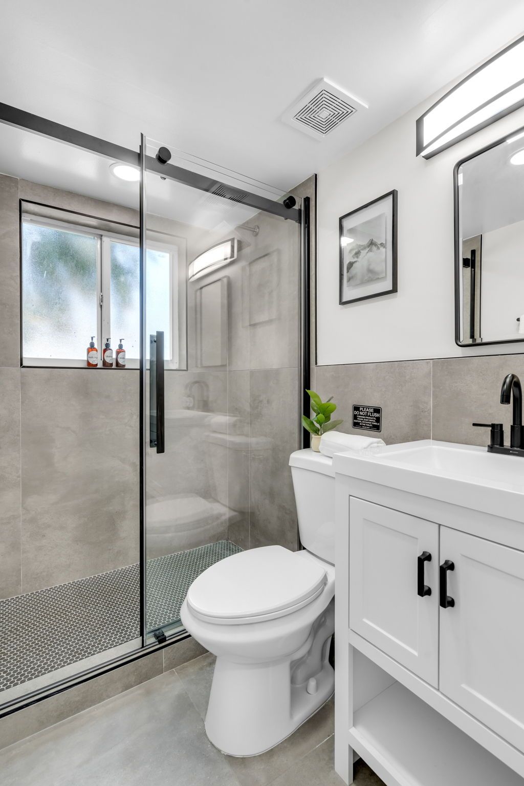 A modern bathroom with a glass shower enclosure, a white toilet, a sink with a mirror, and a cabinet with black handles.