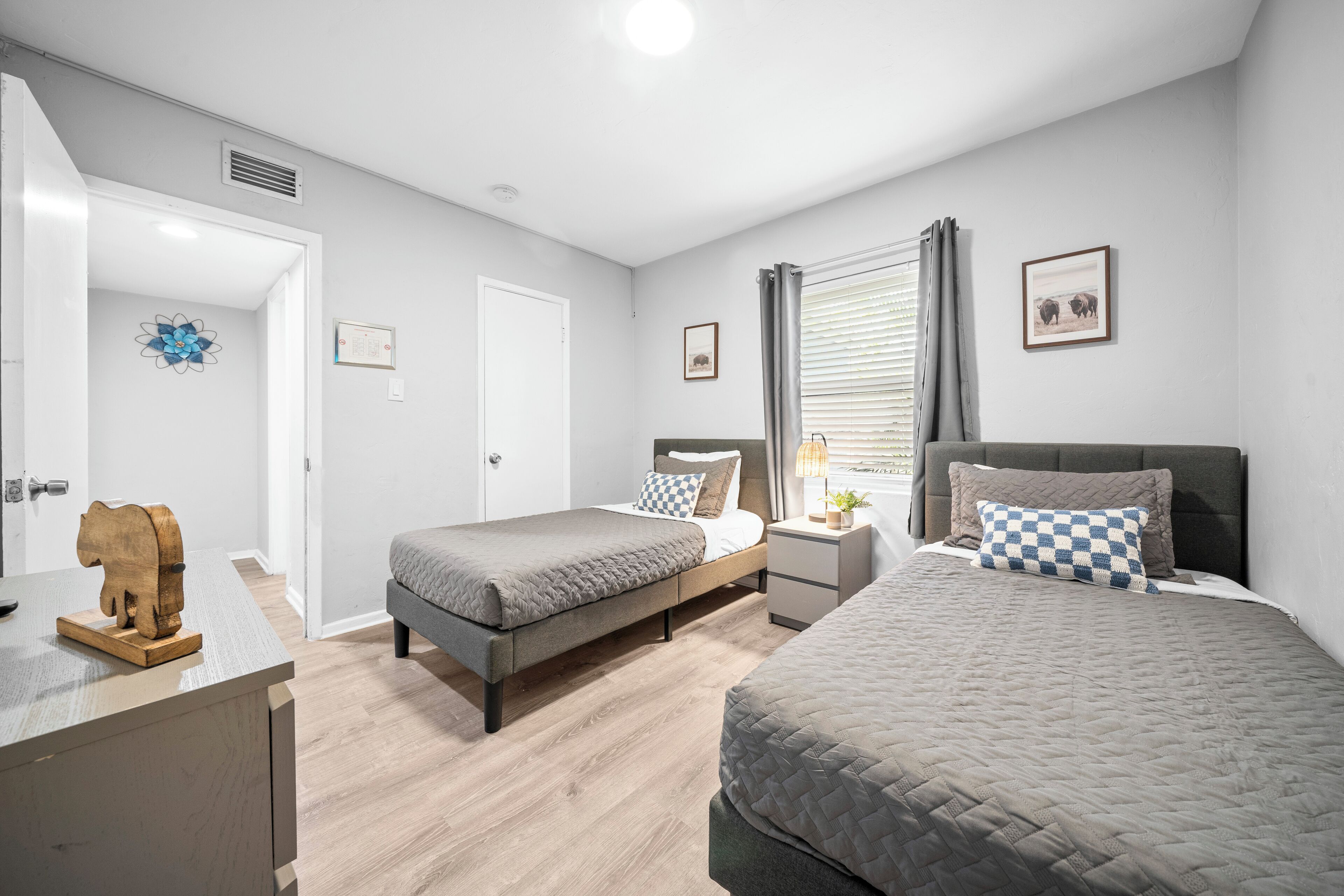 A modern bedroom with two beds, a wooden dresser, and a small desk.