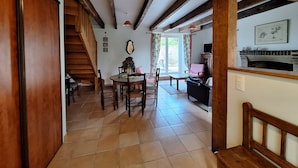 Een ruime woonkamer met een houten trap, een eettafel met stoelen, een open haard en een televisie.