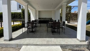 Un patio cubierto al aire libre con una mesa y sillas en el centro, rodeado de pilares blancos.