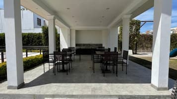 Un patio cubierto al aire libre con una mesa y sillas en el centro, rodeado de pilares blancos.