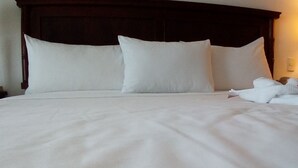 Una cama bien tendida con sábanas y almohadas blancas, un cabecero de madera y un interruptor de pared a la vista.