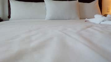 Una cama bien tendida con sábanas y almohadas blancas, un cabecero de madera y un interruptor de pared a la vista.