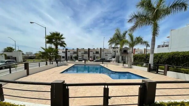 Una piscina con borde de baldosas, rodeada de palmeras y edificios modernos.