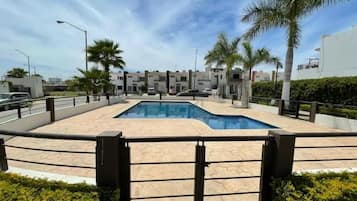 Una piscina con borde de baldosas, rodeada de palmeras y edificios modernos.