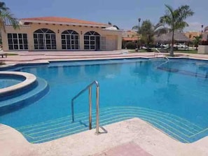 Una piscina con agua cristalina azul, rodeada por una solana con mosaicos y palmeras.