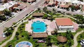 Vista aérea de un complejo turístico con una piscina central, cancha de tenis y un edificio de techo rojo.