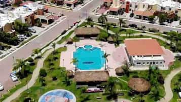 Vista aérea de un complejo turístico con una piscina central, cancha de tenis y un edificio de techo rojo.