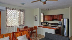 A compact kitchen with wooden cabinets, a stainless steel refrigerator, and a dining area with wooden chairs and a table. - Galeodan Dorado Suite - Spacious Family Suite with Gorgeous Ocean View (Puerto Baquerizo Moreno)