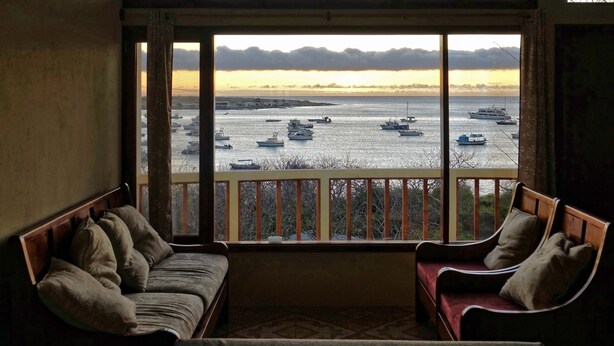 A balcony with a view of boats on the water, a wooden railing, and two cushioned chairs. - Galeodan Dorado Suite - Spacious Family Suite with Gorgeous Ocean View (Puerto Baquerizo Moreno)