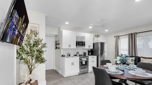 A modern kitchen with white cabinets, a microwave, and a refrigerator. There is a dining table with chairs and a vase of flowers. - Galleria Apartments by Lowkl (Fort Lauderdale)