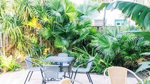 An outdoor patio area with a table and chairs, surrounded by lush tropical plants. - Galleria Apartments by Lowkl (Fort Lauderdale)