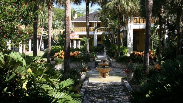 A courtyard with a fountain, palm trees, and a building with balconies. - Galleria Apartments by Lowkl (Fort Lauderdale)