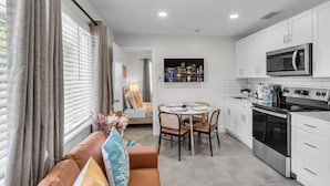 A modern kitchen with white cabinets, a microwave, and an oven. There is a dining area with a table and chairs, and a sofa with cushions. - Galleria Apartments by Lowkl (Fort Lauderdale)