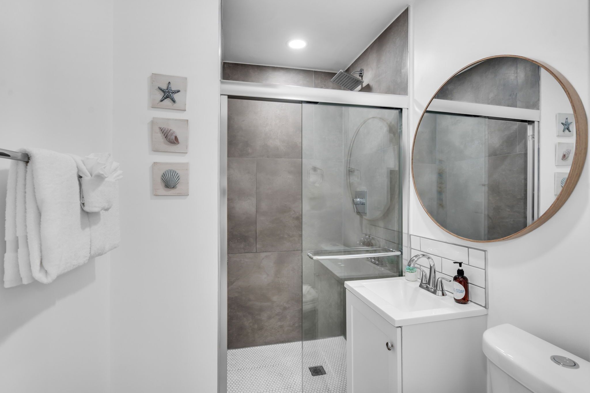 A modern bathroom with a glass-enclosed shower, a white sink, and a round mirror.