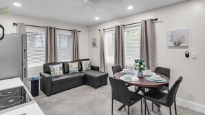 A modern kitchen with a built-in stove, a dining area with a round table and black chairs, and a black leather sofa with decorative pillows. - Galleria Apartments by Lowkl (Fort Lauderdale)