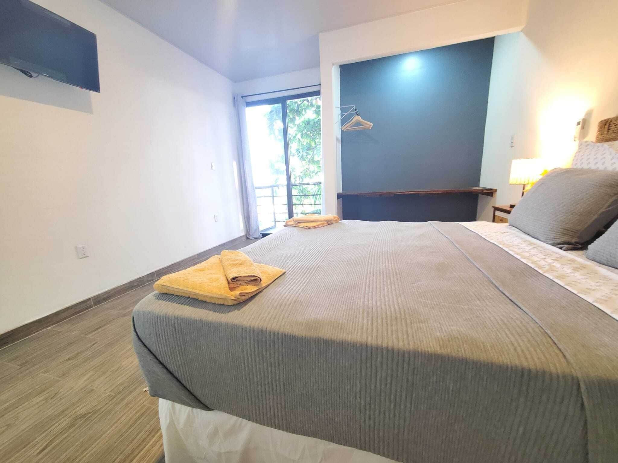 A bedroom with a bed, a window, a TV, and a nightstand with a lamp.