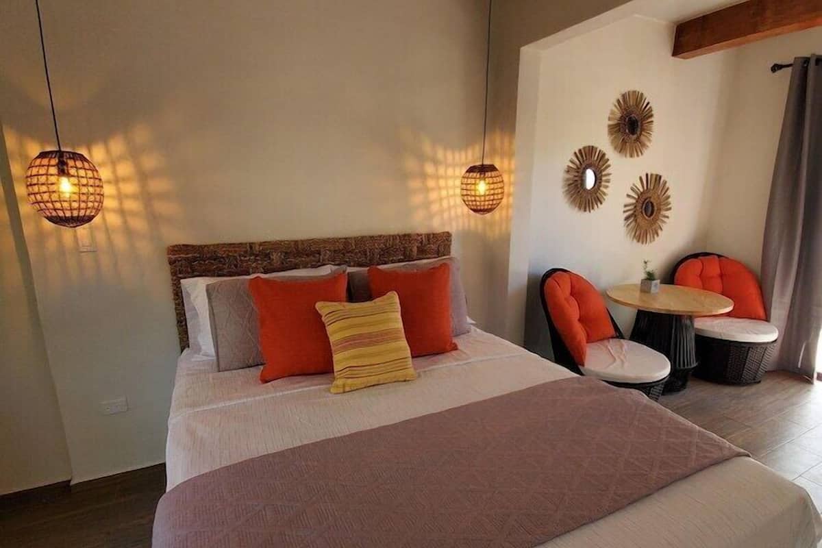 A bedroom with a large bed, two wall-mounted lamps, a small table with chairs, and decorative wall art.