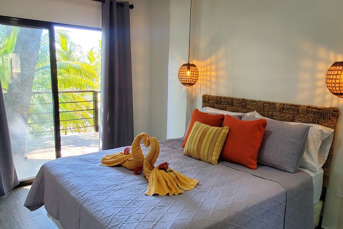 A bedroom with a large bed, a view of palm trees, and a ceiling with exposed beams.