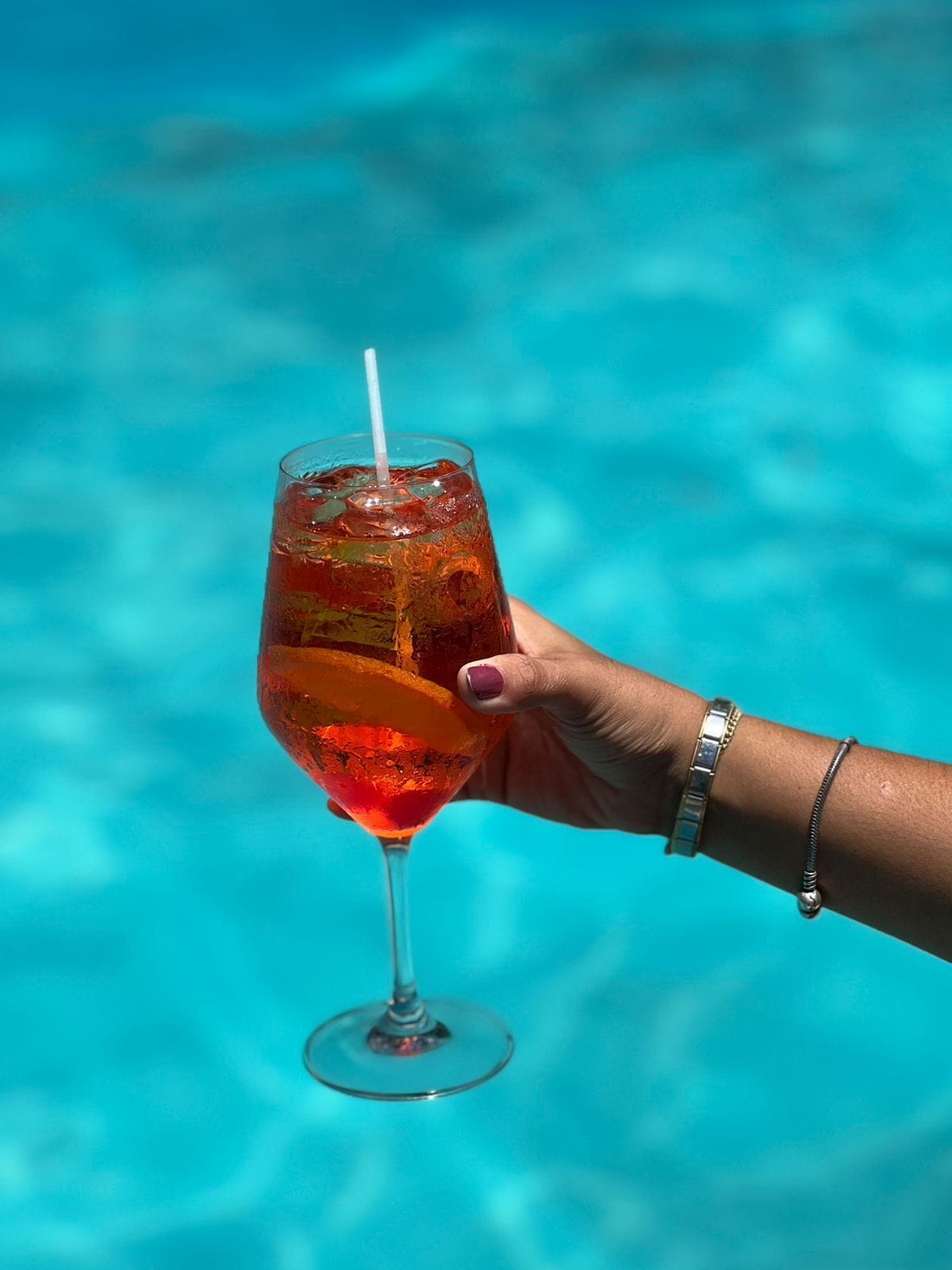 Une main tenant un verre avec une paille, rempli d’une boisson rouge, sur un fond bleu.