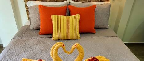 A bed with a quilted bedspread, two swan-shaped towels, and a woven headboard.