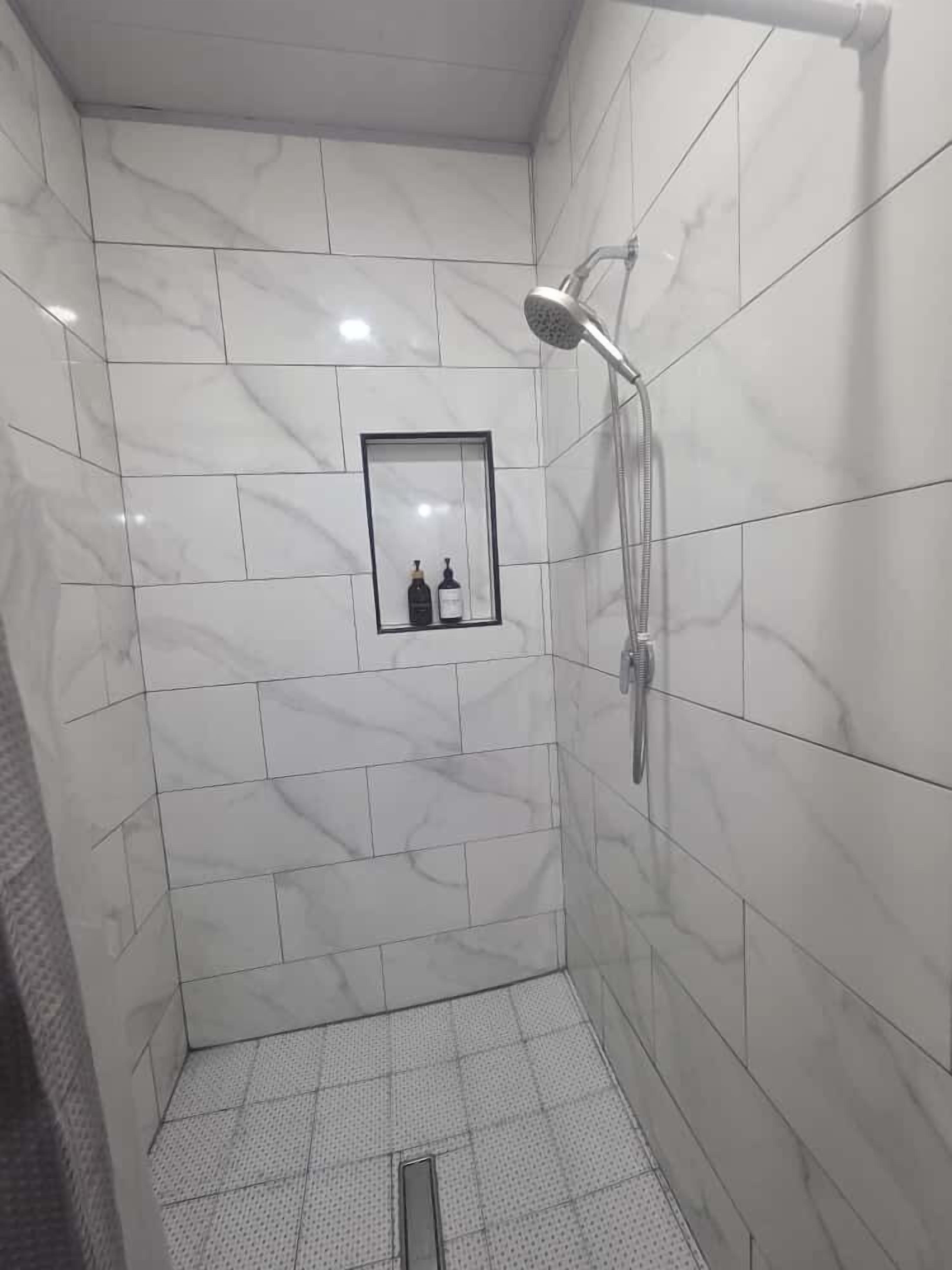 Ein kleines, modernes Duschbad mit weißen Marmorfliesen und einer integrierten Ablage für Pflegeprodukte.