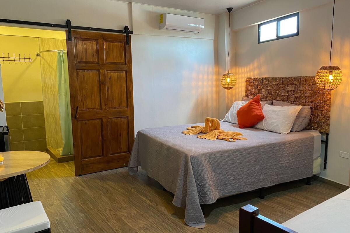 A compact bedroom with a bed, a wooden door, a small table, and a window.