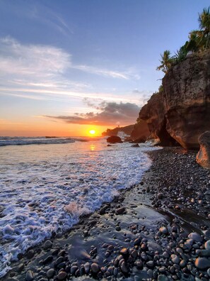 Una playa con piedras y olas al atardecer.