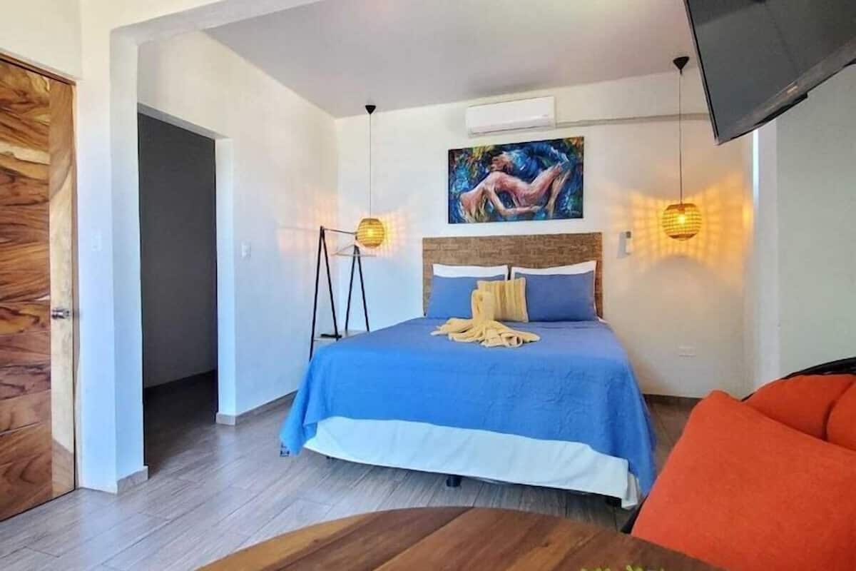 A bedroom with a bed, a TV, a painting, and a plant.