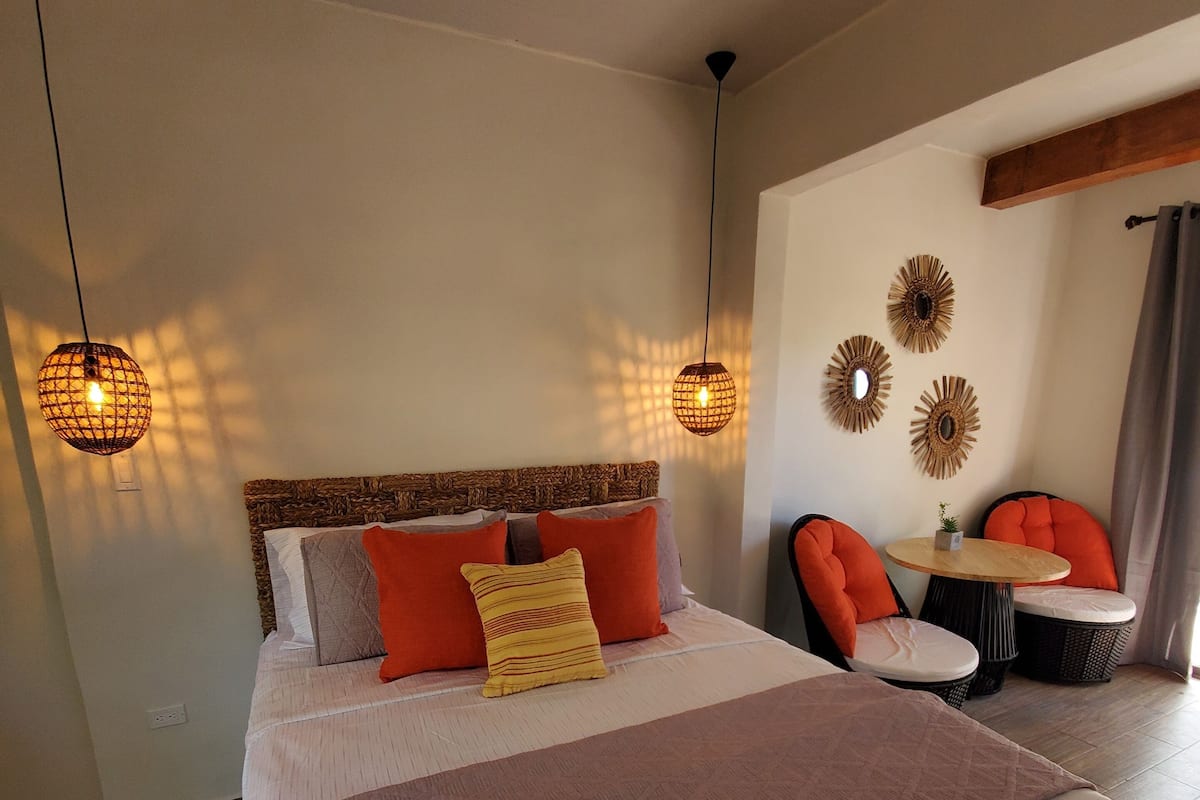 A bedroom with a large bed, two chairs, a small table, and decorative wall art.