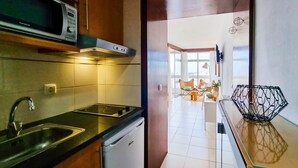 A modern kitchen with a microwave, stove, and sink. There is a dining area with a table and chairs visible through an open door. - FLH Portimão Bright Studio with Balcony (Portimão)