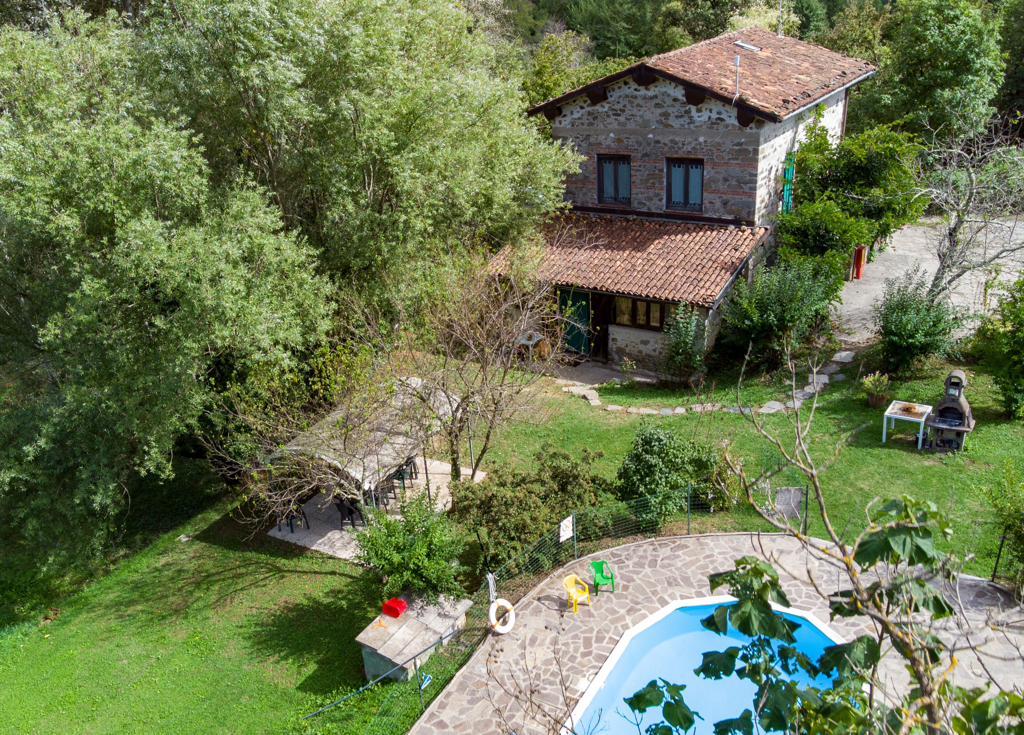 Une maison en pierre avec un toit de tuiles, entourée d’une végétation luxuriante et dotée d’une piscine.