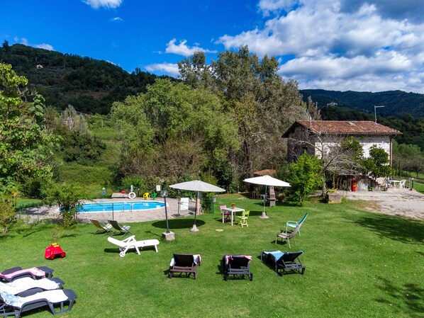 A pool area with lounge chairs, umbrellas, and a stone building.