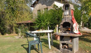 A rustic outdoor dining area with a stone oven, a table, and a chair in a garden setting.