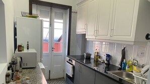Una cocina compacta con armarios blancos, encimera negra y suelo de baldosas.