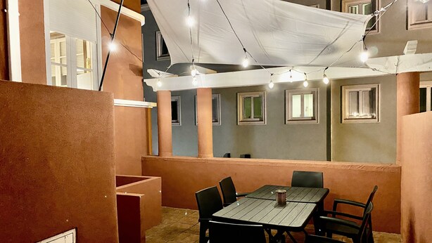 Un área de comedor al aire libre con mesa y sillas, luces colgantes y un toldo blanco.