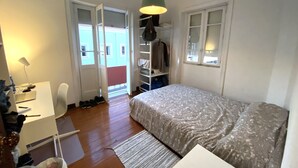 Un dormitorio con cama, escritorio, silla, armario y lámpara colgante.