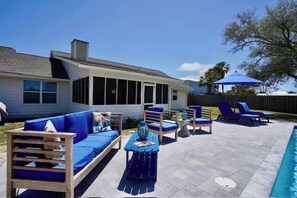 Un jardin avec une piscine, des meubles d’extérieur bleus et un patio couvert.