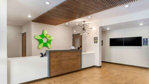 A reception area with a wooden reception desk, a green abstract wall art, a modern chandelier, and a sign indicating room number 1. - Extended Stay America Suites - Atlanta - Mcdonough (McDonough)