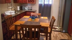 Kompakti keittiö, jossa on puiset kaapit, ruokapöytä tuoleineen, jääkaappi ja mikroaaltouuni.