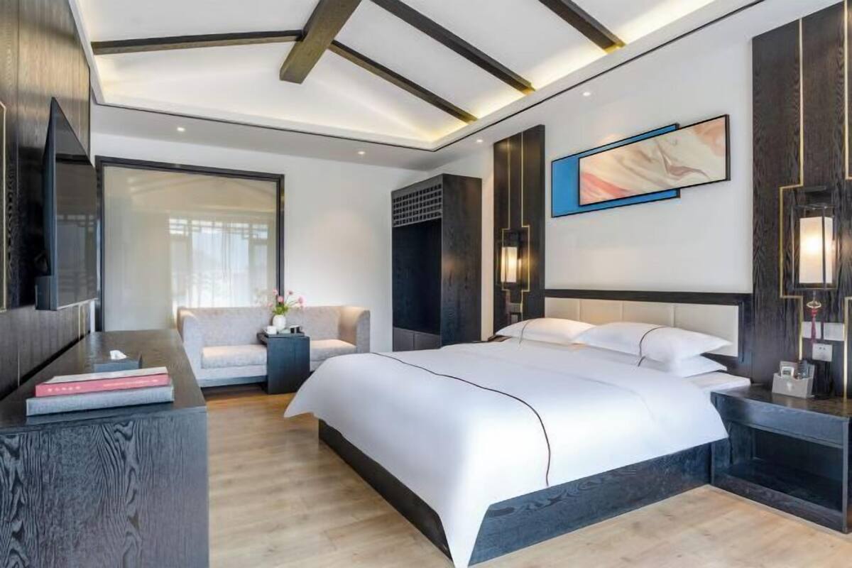 Habitación de hotel moderna con una cama grande, un televisor de pantalla plana, un sofá y un escritorio con un libro.