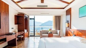 A hotel room with a bed, a desk, a chair, and a balcony with a view of mountains. - Yunti Hotel (Pingbian)
