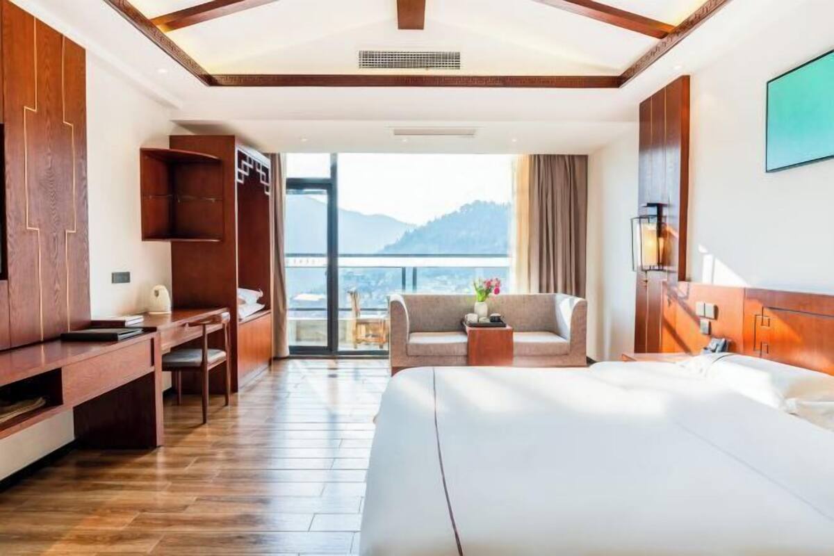 Habitación de hotel con cama, escritorio, silla y balcón con vistas a montañas.