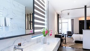 A modern hotel room with a marble bathroom, a large mirror, a vase with flowers, a bed, and a seating area. - Yunti Hotel (Pingbian)