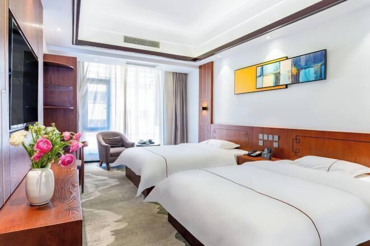 Habitación de hotel con dos camas, un escritorio con un florero, una silla, un televisor y obras de arte en la pared.
