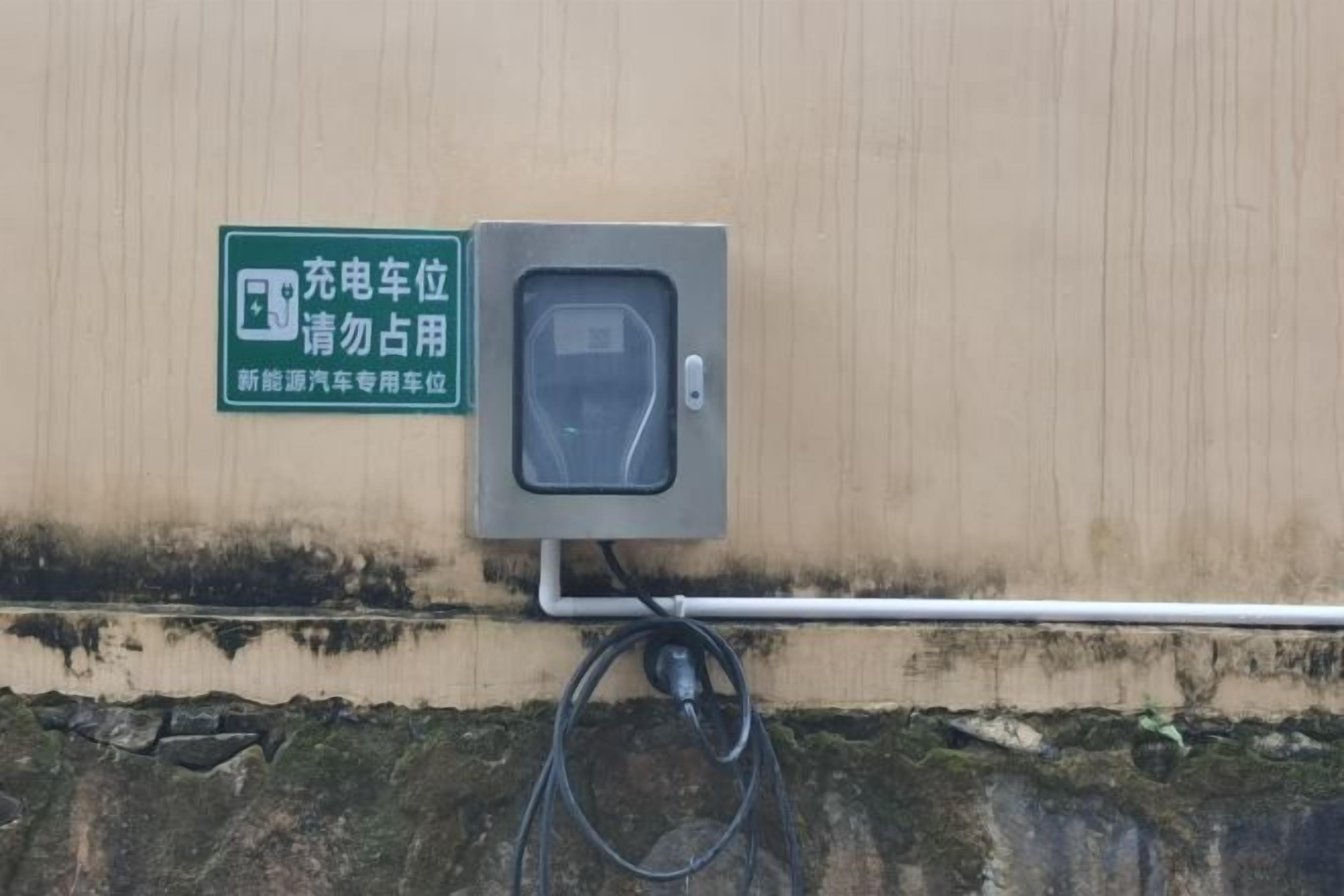 A charging station with a sign, a cable, and a wall-mounted box.