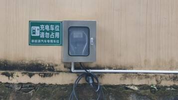 A charging station with a sign, a cable, and a wall-mounted box.
