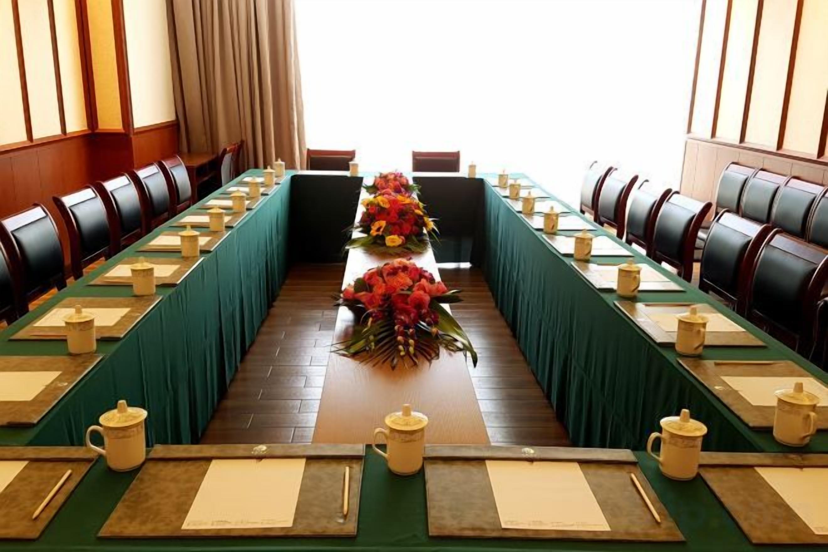 Un salón de conferencias con una larga mesa, sillas y centros de mesa florales.